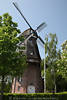 802539_Hinte Mühle Foto, historische Windmühle, Flügel, Galerie, Dorfzentrum, grüne Bäume, Hochformat Aufnahme